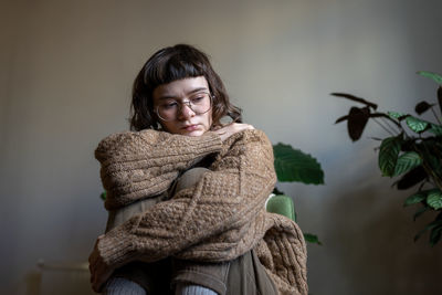 Depressed unhappy teen girl sitting alone at home with knees embraced looking indifferently on floor