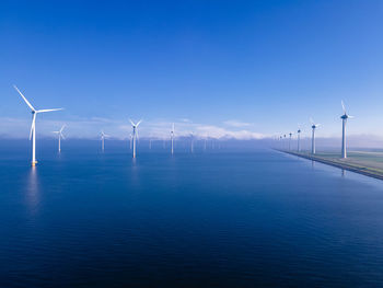 Wind turbines in sea against blue sky