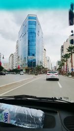 Cars on road by buildings seen through car windshield