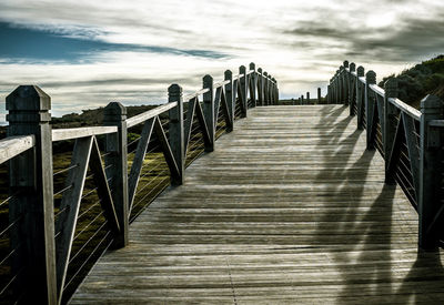 Wooden railing by water against sky