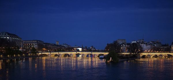 Illuminated city buildings against blue sky at night