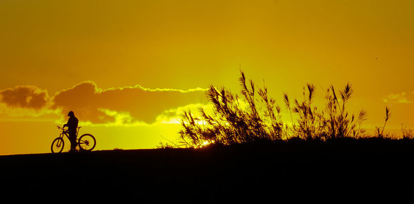 Silhouette person riding bicycle against sky during sunset