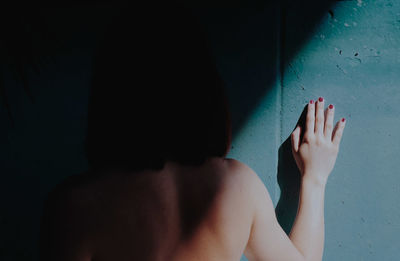 Rear view of shirtless woman standing against wall