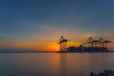 Cranes at commercial dock against sky during sunset