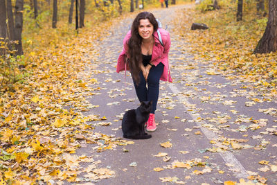 Full length portrait of smiling young woman in autumn leaves