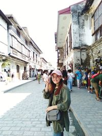 Portrait of young woman showing peace sign while standing on street in city