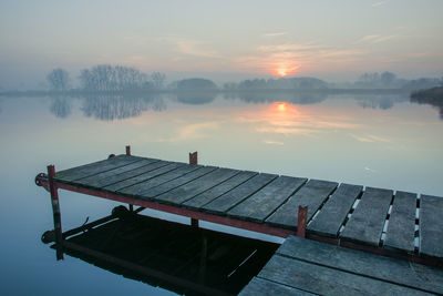 Pier on lake against sky during sunset