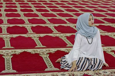 Beautiful woman wearing hijab looking away while sitting on carpet