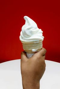 Cropped image of hand holding ice cream against red wall