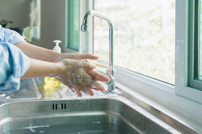 Midsection of woman washing hands in sink