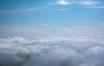 Low angle view of people paragliding against sky