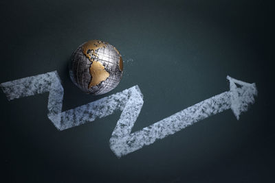 High angle view of globe with upward moving arrow symbol on blackboard