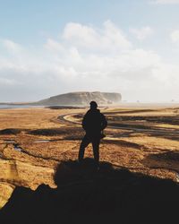 Rear view of man standing on rock against sky