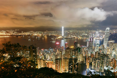 Illuminated city at victoria harbour against sky