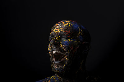 Close-up of mid adult man with body paint screaming standing against black background