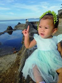 Close-up of cute girl sitting on retaining wall by sea