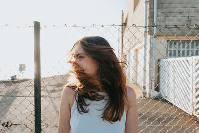 Young woman standing against chainlink fence