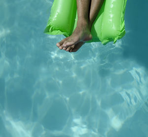 Low section of man relaxing on raft in swimming pool