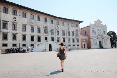 Rear view of young woman walking on street against historic building in city