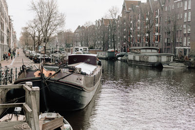 Boats moored in canal by city against sky