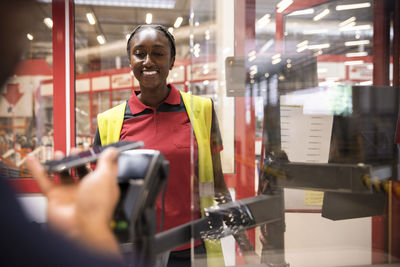 Smiling female sales staff looking at customer doing online payment at checkout counter