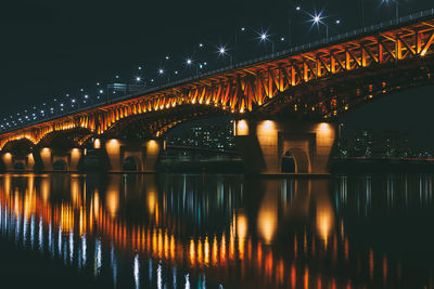 Illuminated bridge over river against sky at night