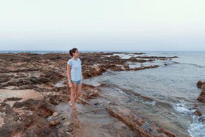 Rear view of woman standing at beach against clear sky