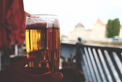 Cropped image of hand holding beer glass at balcony against sky