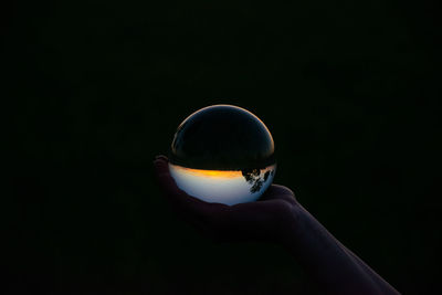 Cropped image of hand holding crystal ball against black background