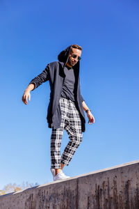 Low angle view of woman jumping against clear blue sky