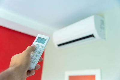 Cropped hand of person operating air conditioner with remote control at home