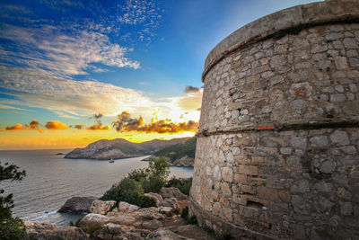 Stone wall by sea against sky during sunset
