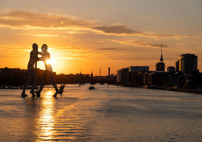 Rear view of man standing by river against sky during sunset