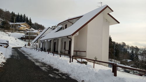 Snow covered houses by building against sky