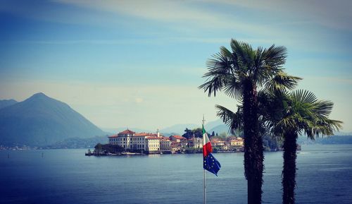 Palm trees and italian and european - eu - flags by sea against sky with island in the background