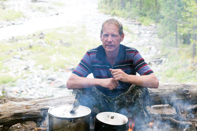 Portrait of man cooking food while sitting in forest