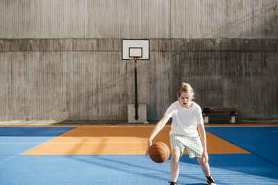 Pre-adolescent girl playing with ball at basketball court