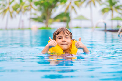 Girl in life jacket gesturing thumbs in swimming pool