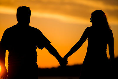 Silhouette couple standing against orange sky during sunset