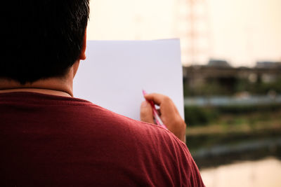 Rear view of man with blank paper in city during sunset