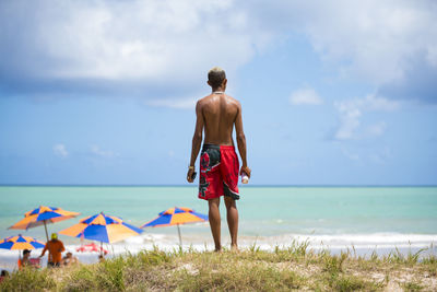 Rear view of shirtless man standing on beach