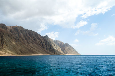 Scenic view of sea by mountains against sky