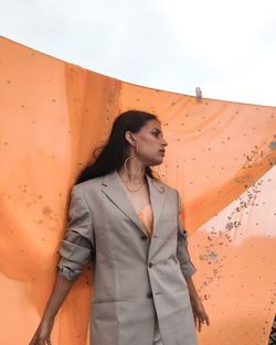 Woman looking away while standing against textile outdoors