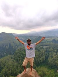 Full length of young man with arms raised against sky