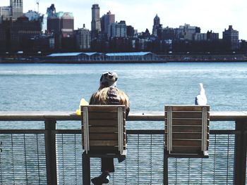 Rear view of woman sitting on chair at railing against river