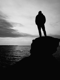 Silhouette man standing on rock by sea