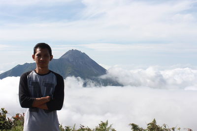 Portrait of young man standing on mountain against sky