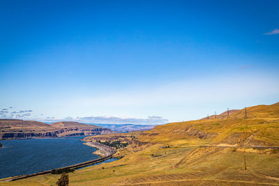 Scenic view of landscape and sea against blue sky