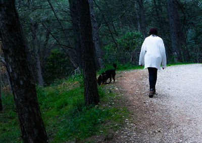 Rear view of woman with dog walking on road in forest