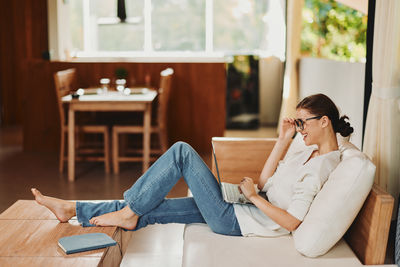 Young woman using mobile phone while sitting on sofa at home